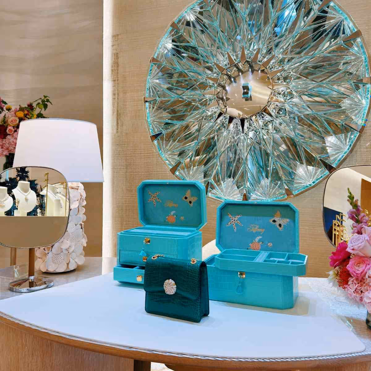 Cajas de joyería turquesa con decoraciones marinas junto a un espejo circular grande