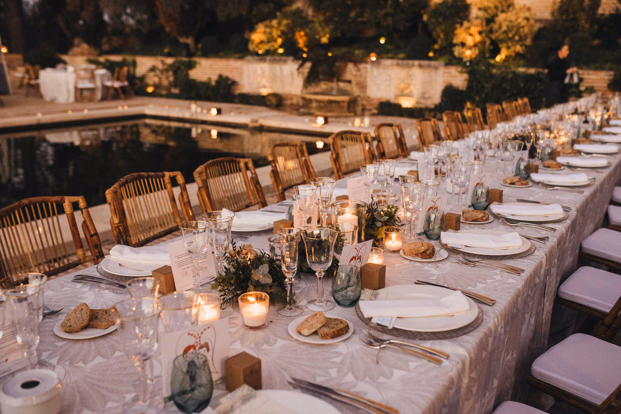 Mesa elegante decorada con velas, flores y vajilla junto a una piscina iluminada