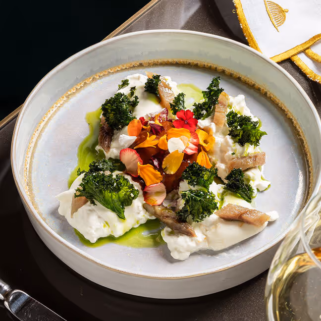 Plato gourmet con brócoli, flores comestibles y salsa verde elegantemente presentado