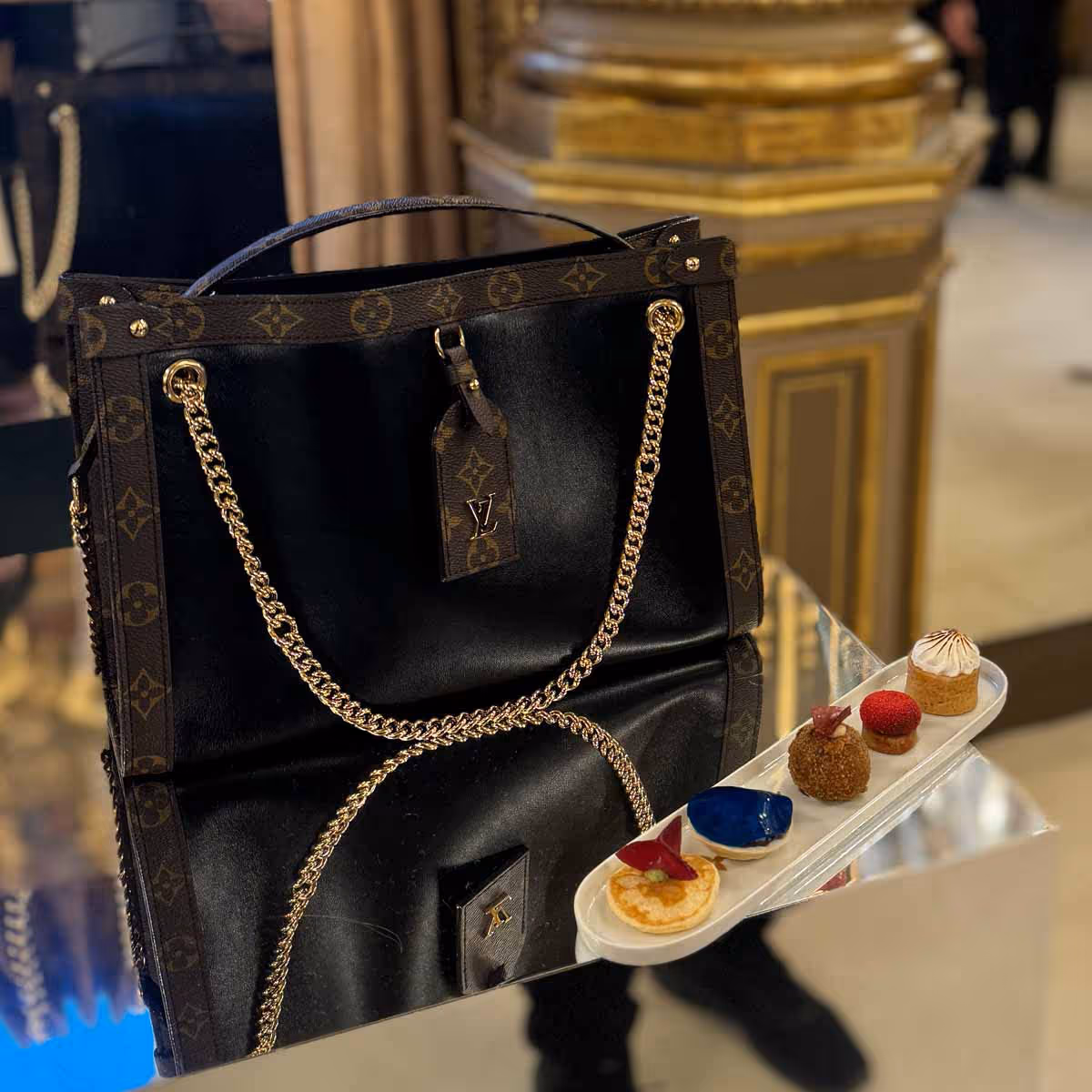 Bolso Louis Vuitton negro con cadena dorada junto a postres elegantes