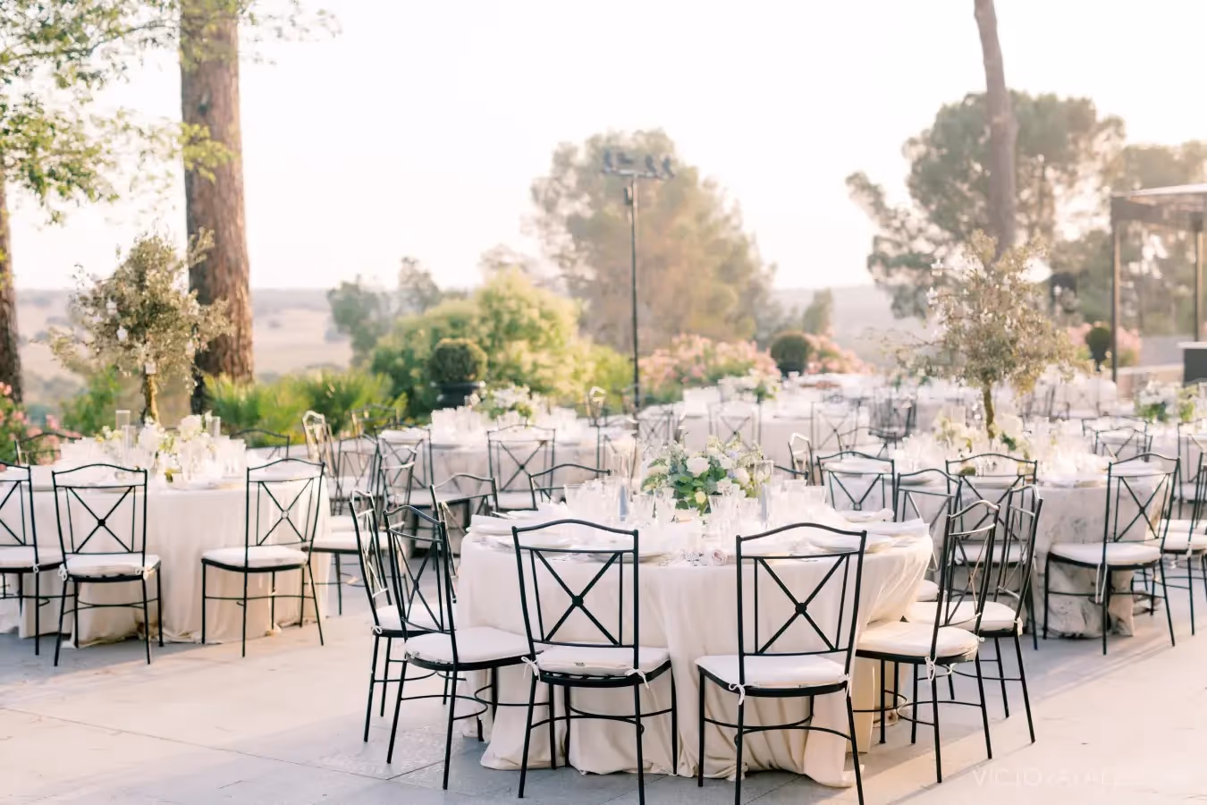 Mesas blancas elegantes para boda con sillas de hierro en jardín soleado