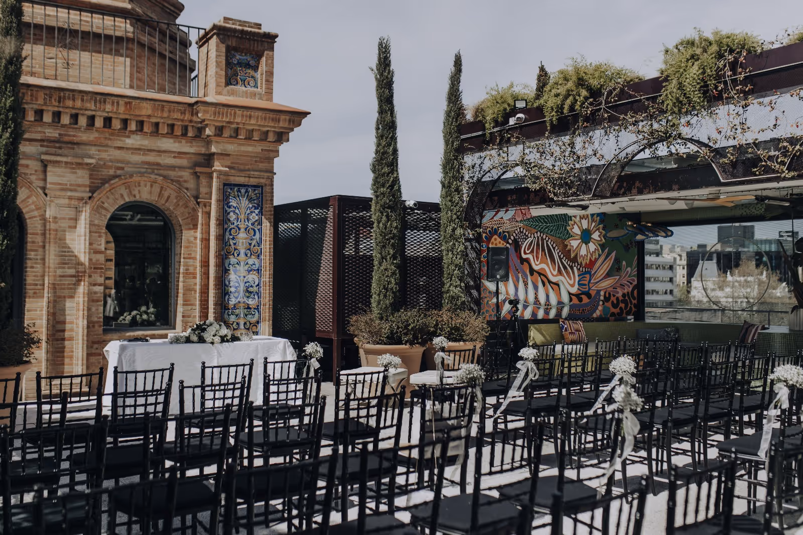 Ceremonia de boda con sillas negras y flores blancas en terraza urbana